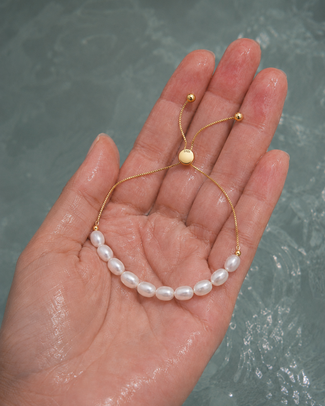 Gouden armband Alba met parels aan een hand ondergedompeld in water