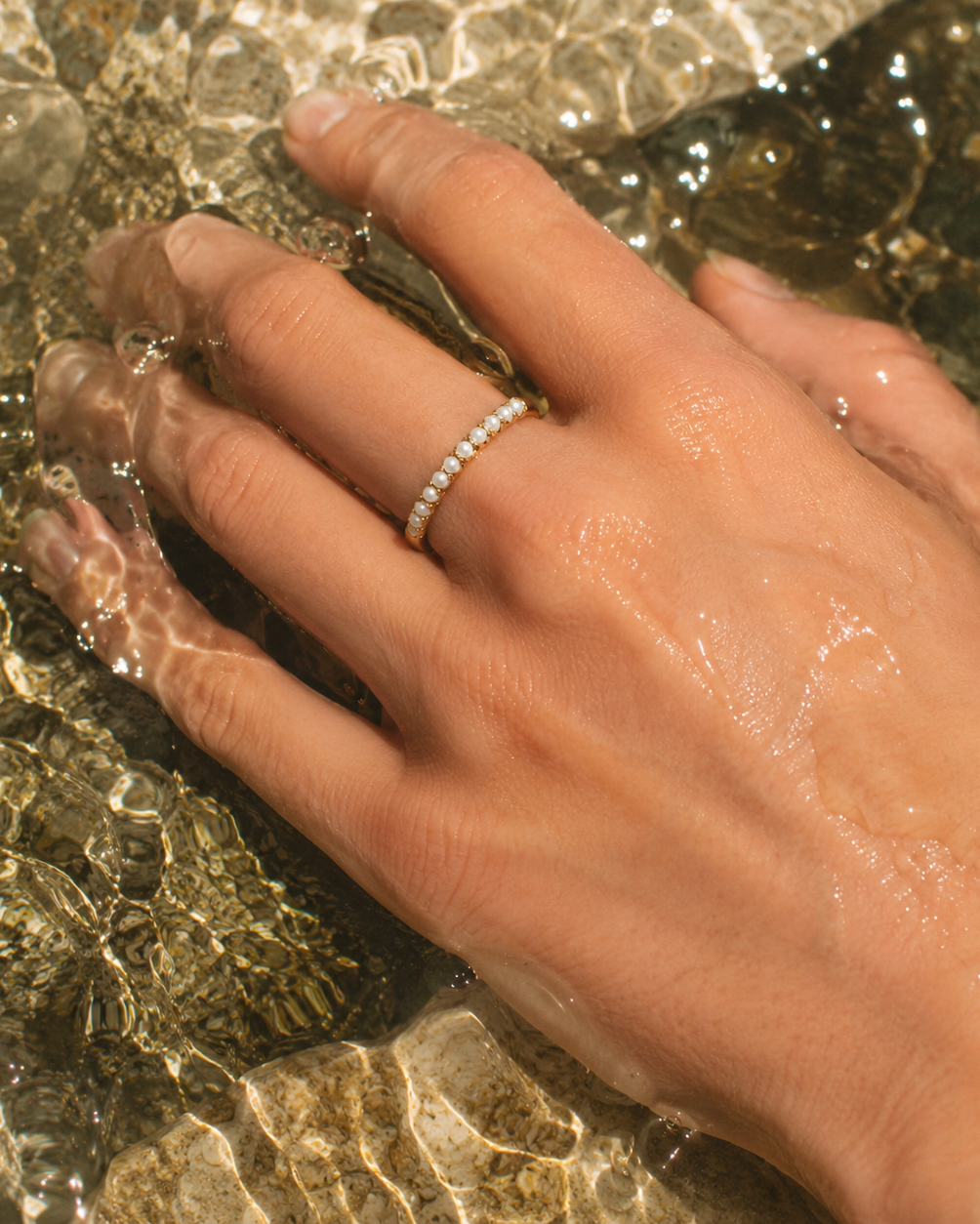Gouden ring Aline met kleine parels aan een hand in het water