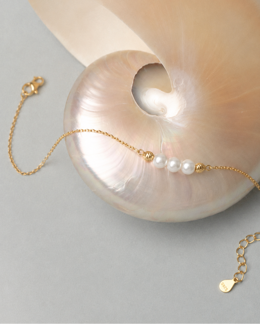 Gouden armband Marea met parels gelegd naast een schelp
