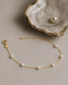Gouden armband Adria met parels gelegd naast een schelp