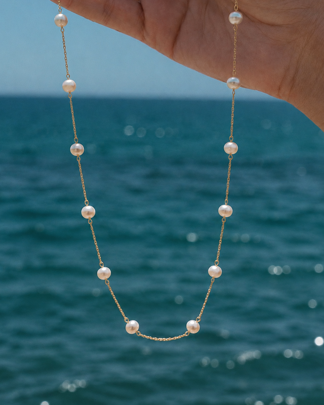 Gouden ketting Adria met parels vastgehouden in een hand aan zee