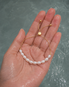 Gouden armband Alba met parels aan een hand ondergedompeld in water