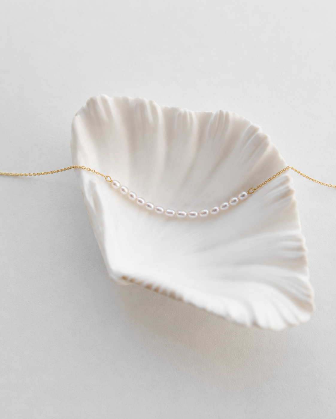 Gouden ketting Aline met kleine parels gelegd op een schelp