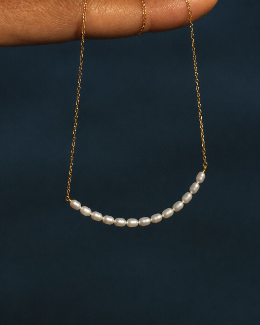 Gouden ketting Aline met kleine parels vastgehouden in een hand boven het water
