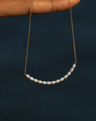 Gouden ketting Aline met kleine parels vastgehouden in een hand boven het water