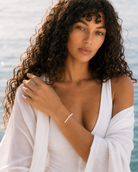 Gouden armband Aurelia met natuurlijke parels en een paperclipketting door een model gedragen aan zee