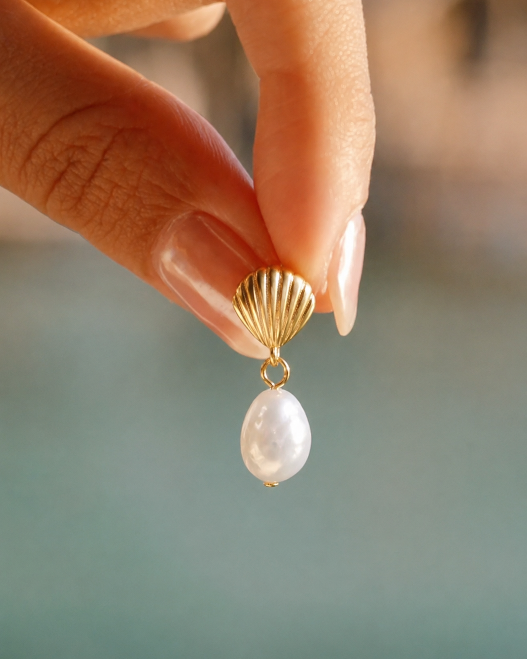 Gouden oorbel Cala met schelpmotief en parel vastgehouden in een hand