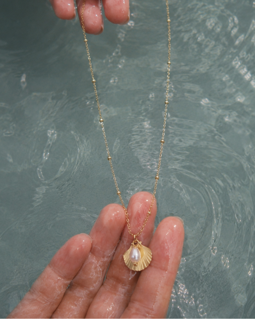 Gouden ketting Cala met een schelp en parel vastgehouden in een hand