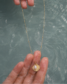 Gouden ketting Cala met een schelp en parel vastgehouden in een hand