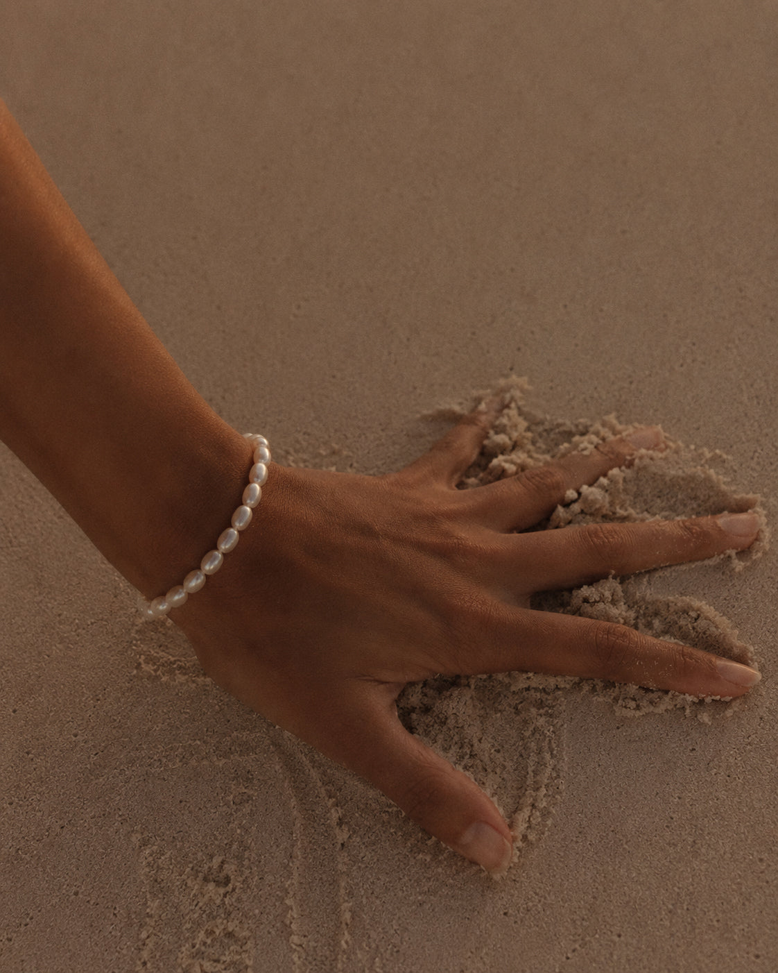 Gouden armband Calista met parels om een pols opartym op het zand
