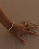 Gouden armband Calista met parels om een pols opartym op het zand