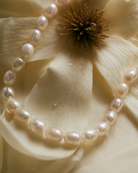 Gouden armband Calista met parels – close-up tegen een bloemrijke achtergrond