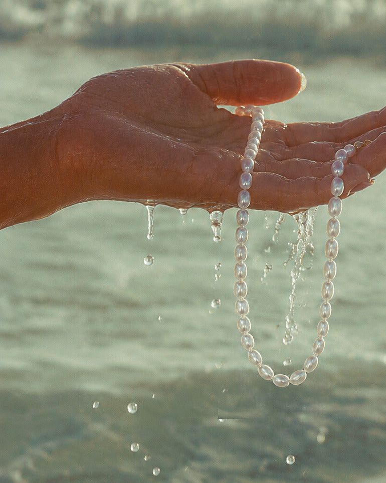 Ketting Calista van onregelmatige parels vastgehouden in een hand in het water