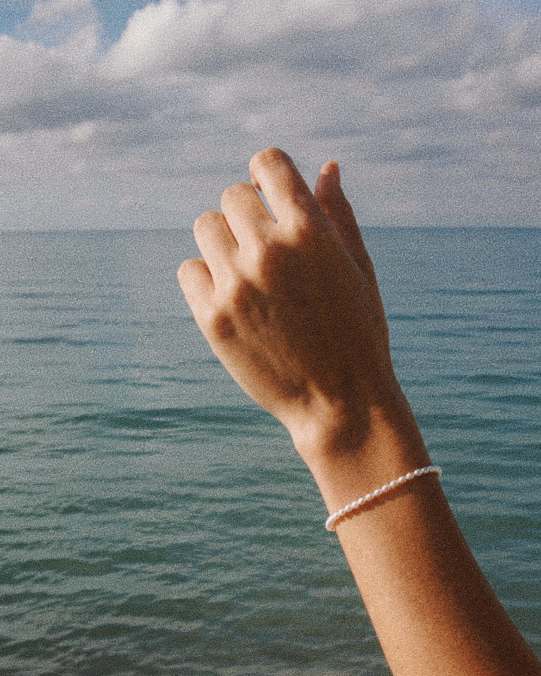 Gouden armband Eira met parels om een pols aan zee