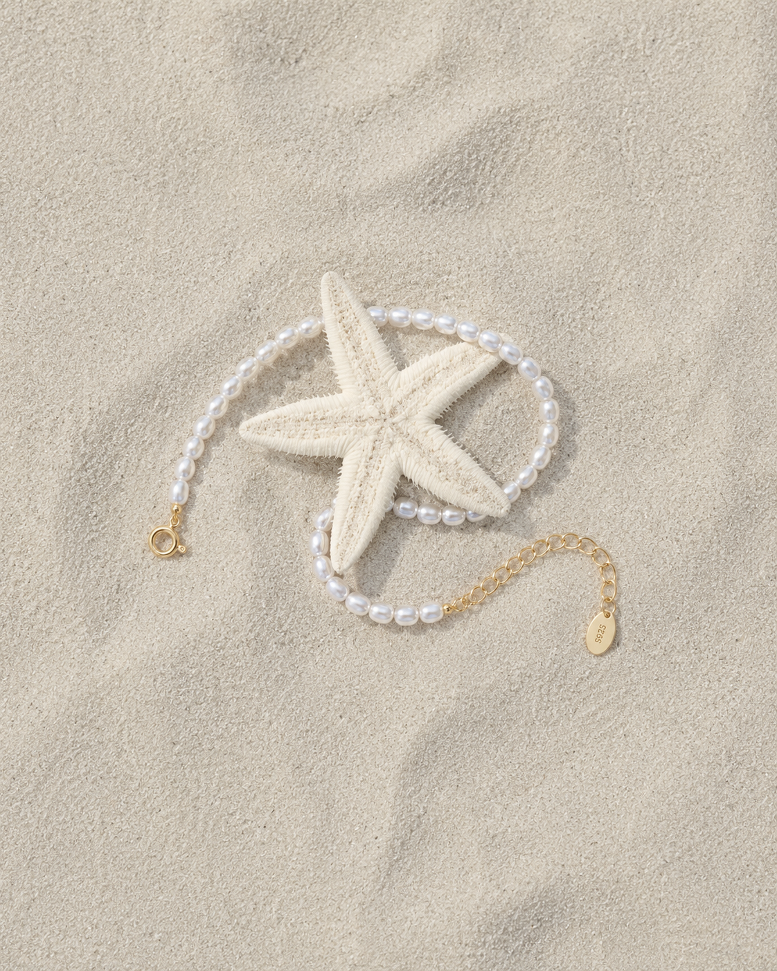 Gouden armband Eira met parels gelegd naast een zeester
