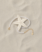 Gouden armband Eira met parels gelegd naast een zeester