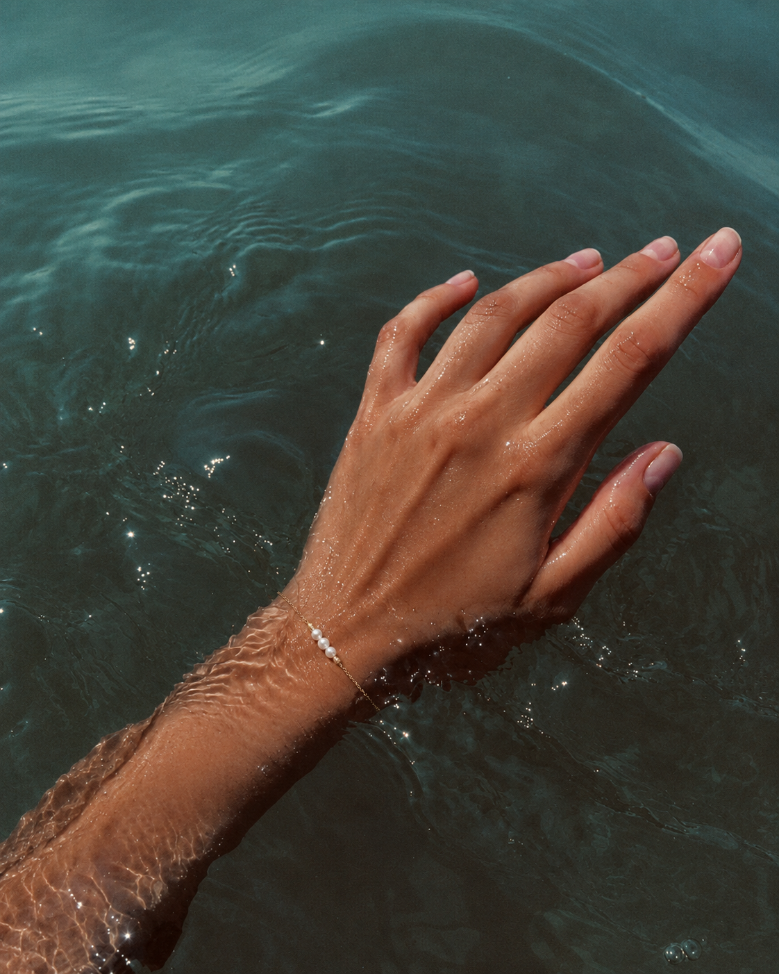 Gouden armband Marea met parels om een pols die in het water is ondergedompeld