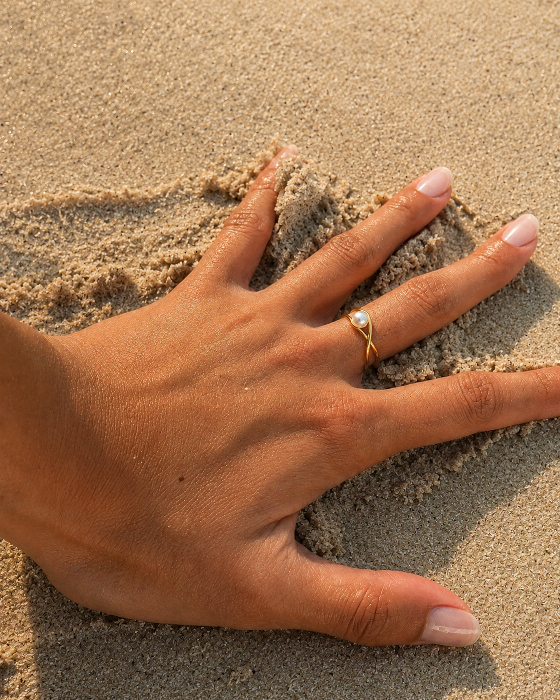 Gouden ring Selene met een parel aan een hand opartej op het zand