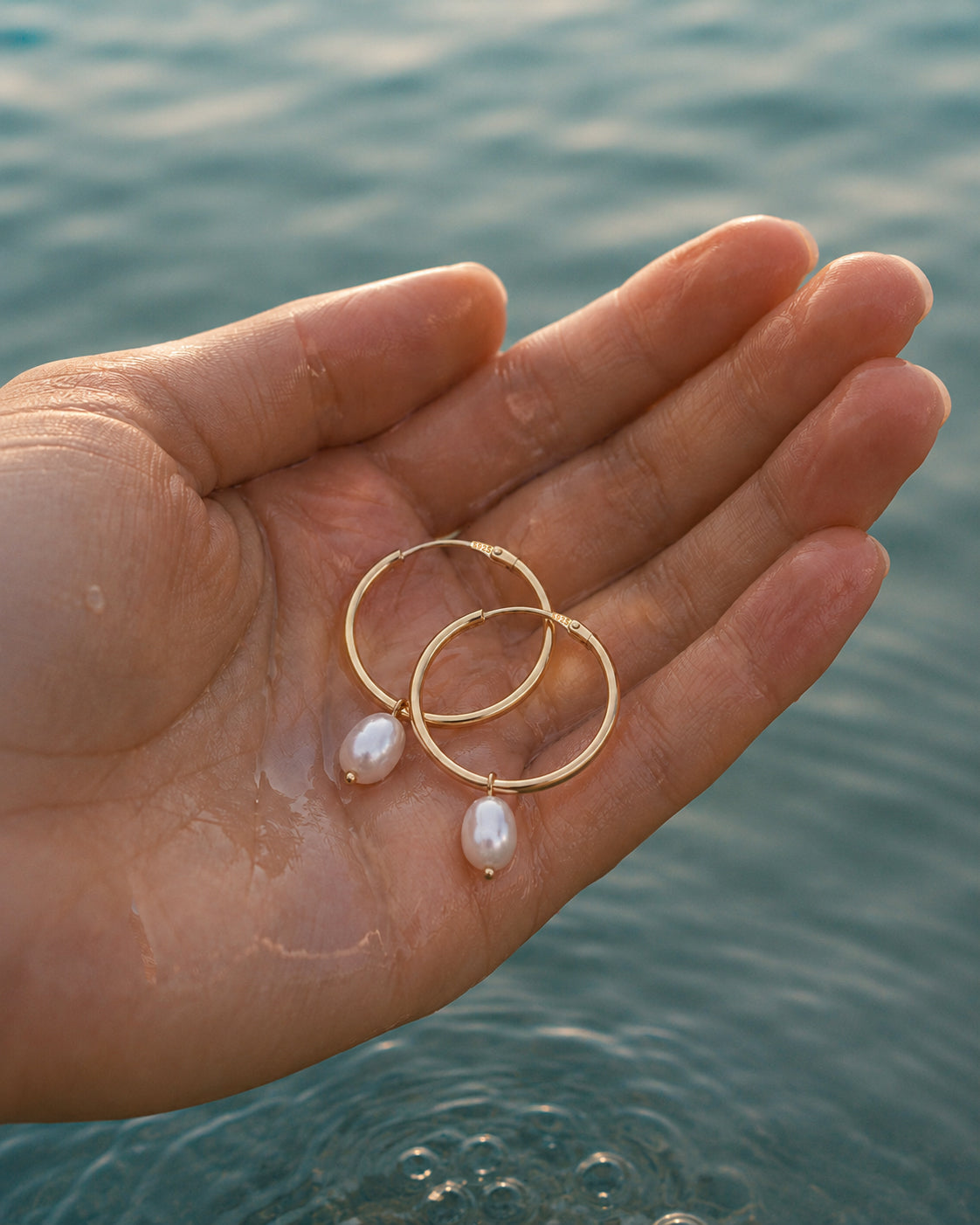 Gouden oorbellen Solea met parels vastgehouden in een hand in het water