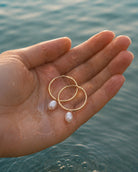 Gouden oorbellen Solea met parels vastgehouden in een hand in het water